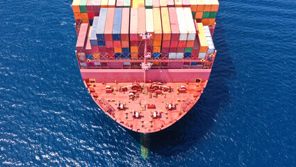 Aerial drone photo of bow from huge fully loaded container tanker ship carrying truck size colourful containers in deep blue open ocean sea