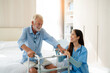 © kelvn - Care worker helping elderly man get out of bed and walk around the room.