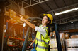 © kelvn - Asian women staff worker in uniform and yellow helmet in warehouse, smiling and waving somebody greetings.