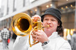© pavelgulea - Young caucasian hally cheerful man in white shirt and hat playing funky jazz on golden trumpet with pleasure standing on crowded blurred downtown street close up. Musical lifestyle, hobby, education