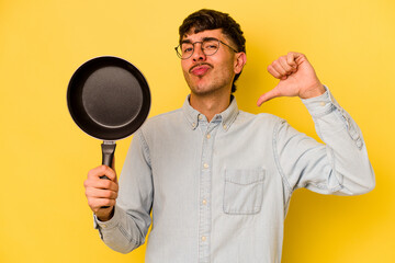 Wall Mural - Young hispanic cooker holding frying pan isolated on yellow background feels proud and self confident, example to follow.