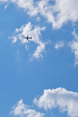 Wall Mural - The passenger airplane is flying far away in the blue sky and white clouds. Aircraft in the air. Light vertical background or illustration about international passenger air transportation