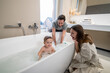 © zinkevych - Child looking at camera in bathtub and parents watching