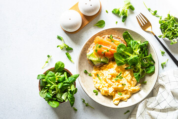 Canvas Print - Scrambled eggs, sandwich with cream cheese and salmon and salad leaves at white stone table. Top view.