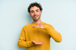 © Asier - Young caucasian man isolated on blue background holding something with both hands, product presentation.