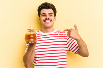 Young caucasian man holding honey jar isolated on yellow background person pointing by hand to a shirt copy space, proud and confident