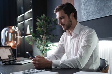 Sticker - Smiling businessman holding smartphone sitting in office. Middle aged manager ceo using cell phone mobile apps