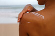 closeup woman applying sunblock cream lotion on beach for broad spectrum UVA, UVB sun protection