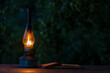 Old antique burning kerosene lamp with open book on the wooden table, copy space