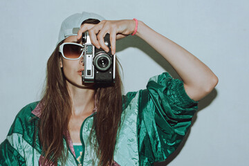 Cool teenager. Fashionable girl in colorful trendy jacket and vintage retro sunglasses with camera film in 80s - 90s style. Teenage girl at the disco, on a white background.