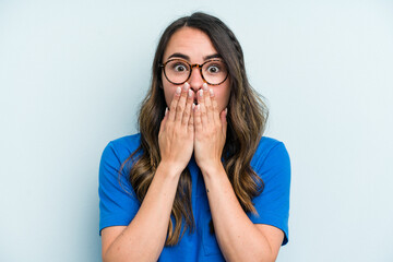 Wall Mural - Young caucasian woman isolated on blue background shocked, covering mouth with hands, anxious to discover something new.