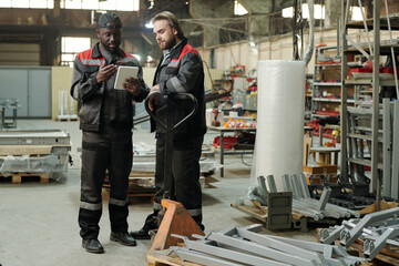 Aufkleber - Young black man in workwear making presentation of new construction materials to his colleague during working meeting in warehouse