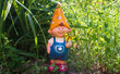 Funny cute colorful garden gnome stands in the garden green grass. Garden dwarf with little butterfly in his hand. Decorative sculpture.