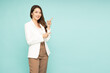 © comzeal - Young beautiful Asian businesswoman smiling and pointing to empty copy space isolated on green background