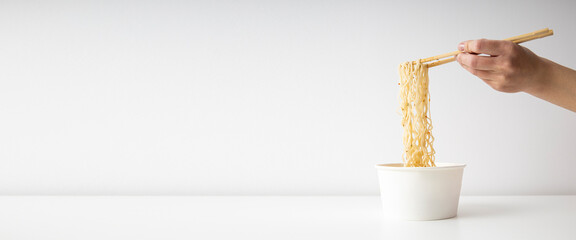 Female hand takes Chinese noodles with Chinese chopsticks from a paper bowl on a white background. Banner