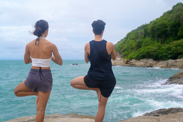 Young man and woman in sportswear doing yoga on the rock at seaside, health and meditation concept