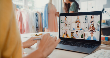 Close-up young Asia lady dressmaker use laptop on meeting with multi graphic designer team discuss sample create dress design new collection on desk in shop. Tailor new business startup concept.