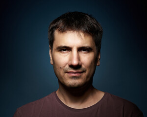 Wall Mural - Portrait of a 42-year-old brunette man on a dark background with bright illumination