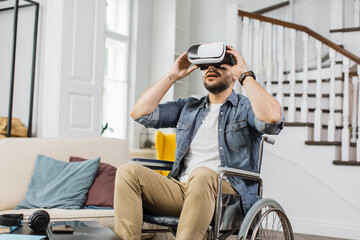 Disabled man watching virtual video using goggles of augmented reality while sitting in wheelchair at home. Concept of full technology opportunities for people with special needs.