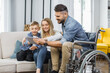 © sofiko14 - Caucasian man in wheelchair and his lovely wife with cute son watching video on digital tablet at home. Concept of family, disability and technology.