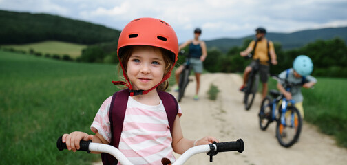 Wall Mural - Portrait of excited little girl with his family at backround riding bike on path in park in summer