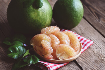 fresh green pomelo peeled and leaf frome pomelo tree , pummelo , grapefruit in summer tropical fruit  in thailand , pomelo fruit on wooden plate background