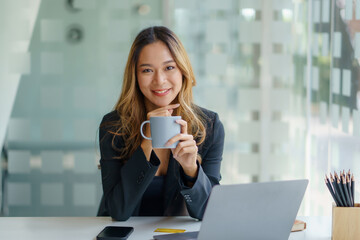 Wall Mural - Happy Asian businesswoman sitting holding coffee cup in office.