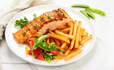 Canvas Print - Salmon steak with vegetables and fries on light background.