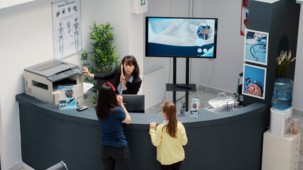 Wall Mural - Diverse group of patients waiting to attend medical appointment, sitting at busy hospital reception desk. People with healthcare insurance having examination with specialist. Handheld shot.