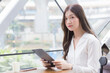 © nut_foto - Professional beautiful young Asian business woman is looking at camera in her hands tablet or notepad while she is sitting at coffee shop among business background in the city.