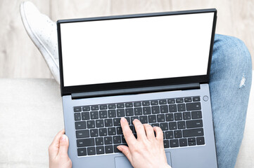 Poster - Top view mockup image of woman holding laptop with blank white screen. woman using notebook with while sitting cross-legged on sofa at home. Mockup laptop