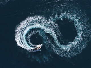 Aerial top view of a white pleasure boat on a summer day. Powerboat turn loop eight on the sea making metaverse infinity future concept. 