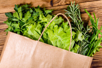 Wall Mural - Paper bag with lettuce rosemary and parsley on a wooden table. Vegan food. Top view