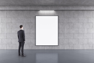 Poster - Advertising concept with businessman back view looking at blank white poster in black frame with space for your logo or text on grey concrete wall in subway with glossy floor, mock up