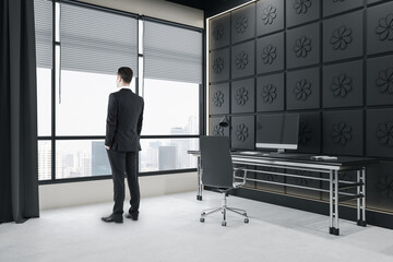 Aufkleber - Thoughtful young man standing in modern dark concrete coworking office room interior with window, city view, curtains and furniture. Ceo and boss concept.