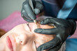 © dtatiana - Procedure of eyebrow microblading. A master in black gloves is doing a blending needle of model's brow.