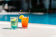 Tropical sparkling lemonade cocktails by the pool. Glasses with orange and mint lemon fruit cocktails. Summer alcohol free drink by the hotel pool. Hello summer holiday vacation