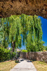 Wall Mural - A glimpse of the medieval village of Bevagna. Perugia, Umbria, Italy. Blue sky in a sunny summer day. The big weeping willow below the masonry bridge.