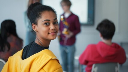 Sticker - College student sitting in school-desk and looking at camera.