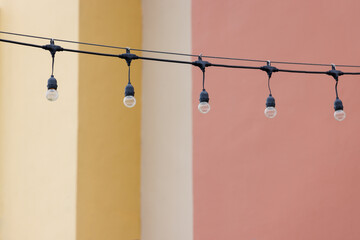 Wall Mural - string wired bulbs decoration outdoor of building. garland of a light bulbs with the yellow and pink concrete wall background.