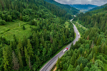 Wall Mural - red cargo truck on the higthway. cargo delivery driving on asphalt road through the mountains. seen from the air. Aerial view landscape. drone photography.
