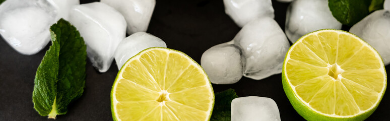 Wall Mural - high angle view of melting ice cubes near sliced limes and milt leaf on black background, banner.