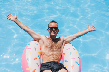 A young man in sunglasses and shorts is relaxing on an inflatable donut in the pool. Summer vacation