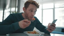 Blond athletic man eating his breakfast and looking at phone in the kitchen
