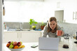 © Wavebreak Media - Caucasian mid adult lesbian woman holding coffee mug and using laptop on kitchen island, copy space
