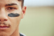 Portrait of a young male baseball player standing on a field with black paint markings on his face. Focused skilled sportsman, determined and motivated to have a competitive sporting game outside