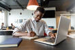 © wavebreak3 - Smiling young african american businessman writing in diary and using laptop in creative office