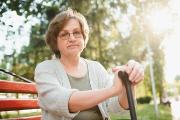 Canvas Print - An elderly woman sitting on bench in summer park