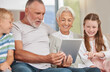 © Beaunitta V W/peopleimages.com - A happy mature couple bonding with their grandchildren while babysitting and using a digital tablet at home. Grandparents relaxing with their cute little grandson and granddaughter browsing internet