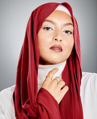 Wall Mural - Portrait of a Muslim woman wearing a red hijab or headscarf showing her eyelash extensions and makeup. Showing her flawless skin glowing. Beautiful woman isolated against a grey studio background.